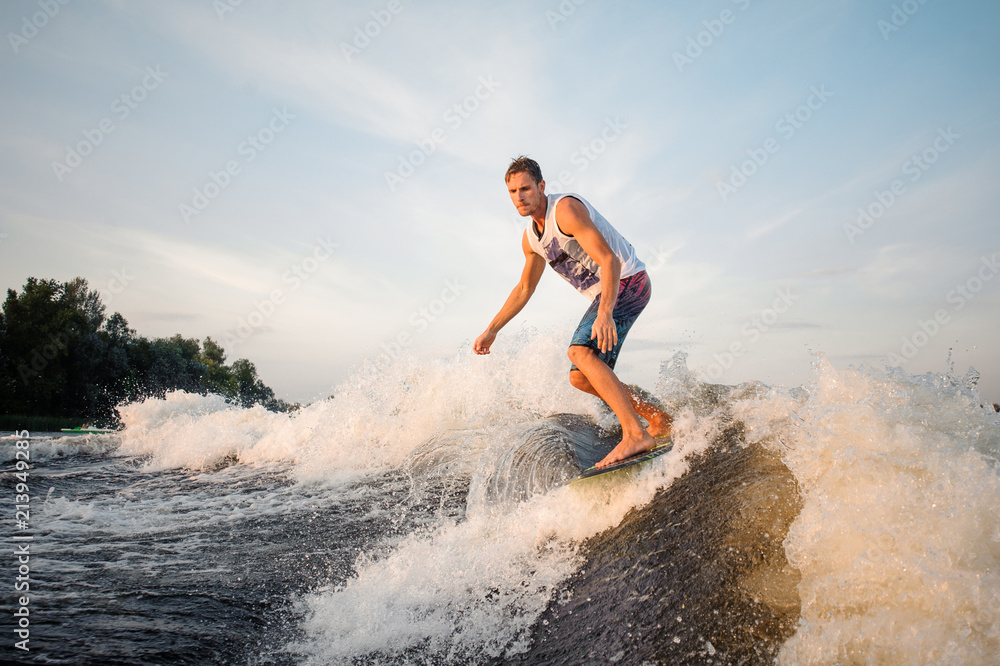 Muscular wakesurfer riding down the river on board