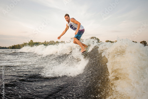 Athletic wakesurfer jumping on board riding down the river waves