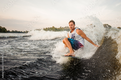 Handsome wakesurfer riding down the river on board