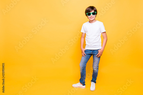 Full height portrait of attractive young cheerful school boy, smiling, wearing sun glasses standing over yellow background, isolated. Copy space