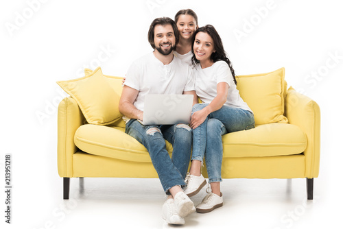 smiling family with laptop sitting on yellow sofa isolated on white