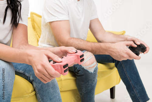 partial view of couple with gamepads sitting on sofa isolated on white