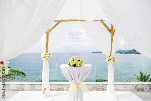 Fototapeta Naklejka Na Ścianę i Meble -  Close-up wedding arch decorated with white soft lawn fabric and color roses flower bouquet on the altar, beautiful nature coastal background