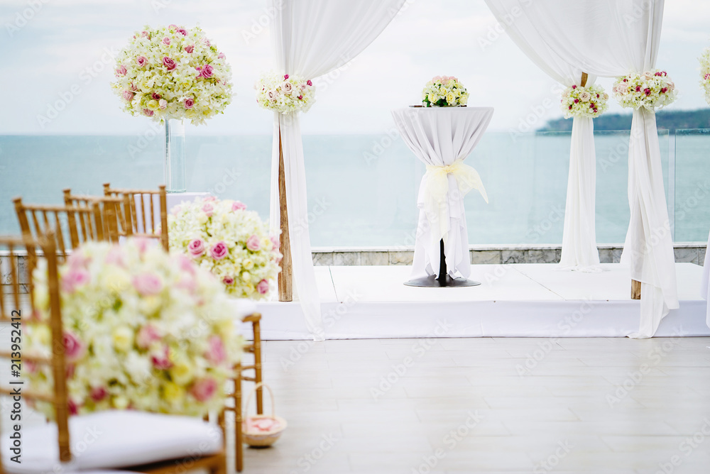 Fototapeta premium Wedding arch and altar decorated with white lawn fabric and roses, flowers, floral and green leaf with ocean view background