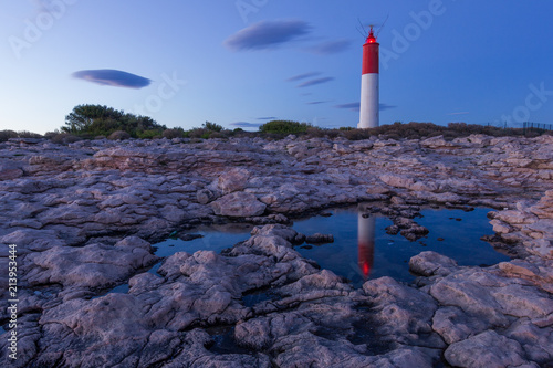 Quiet evening by a lighthouse on rocky shore. Building reflected in a pond. Amazing colorful sunset with only few clouds in the sky.