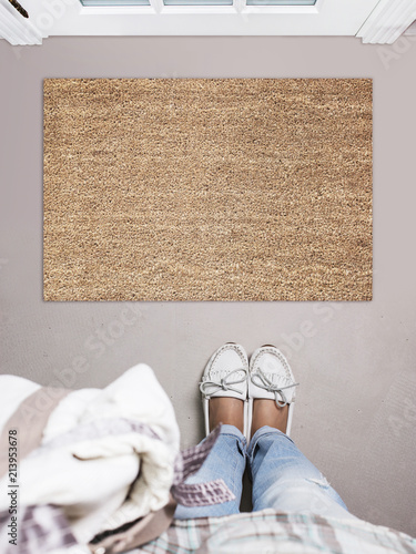 Blank doormat before the door in the hall. Mat on gray floor, girl in white shoes. Welcome home, product Mockup