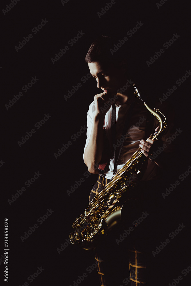 Obraz premium pensive young musician holding saxophone isolated on black