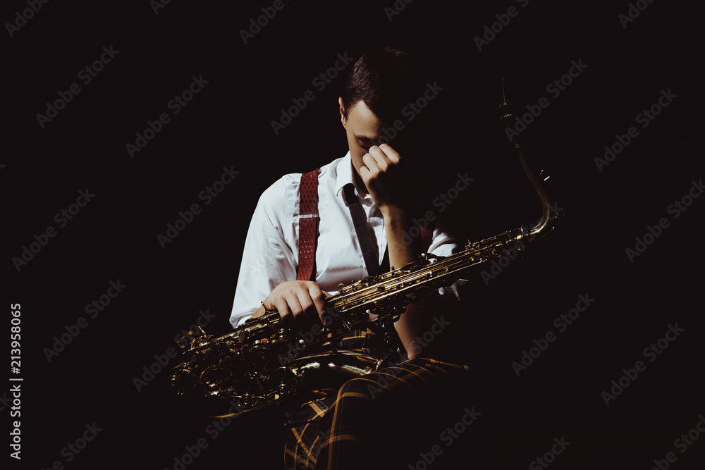 Naklejka premium young musician holding saxophone isolated on black