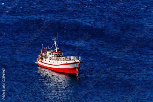 Aerial view of red fishing boat on a deep blue sea in Greece.