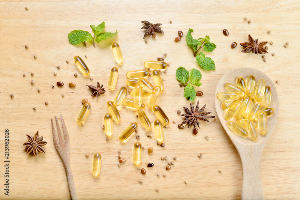 Medicine herb, Cod liver oil omega 3 gel capsules on wooden spoon and fork with healthy medicinal plant on top wooden brown tone background. Medicine herb, Cod liver oil omega 3 gel capsules on wooden spoon and fork with healthy medicinal plant on top wooden brown tone background.