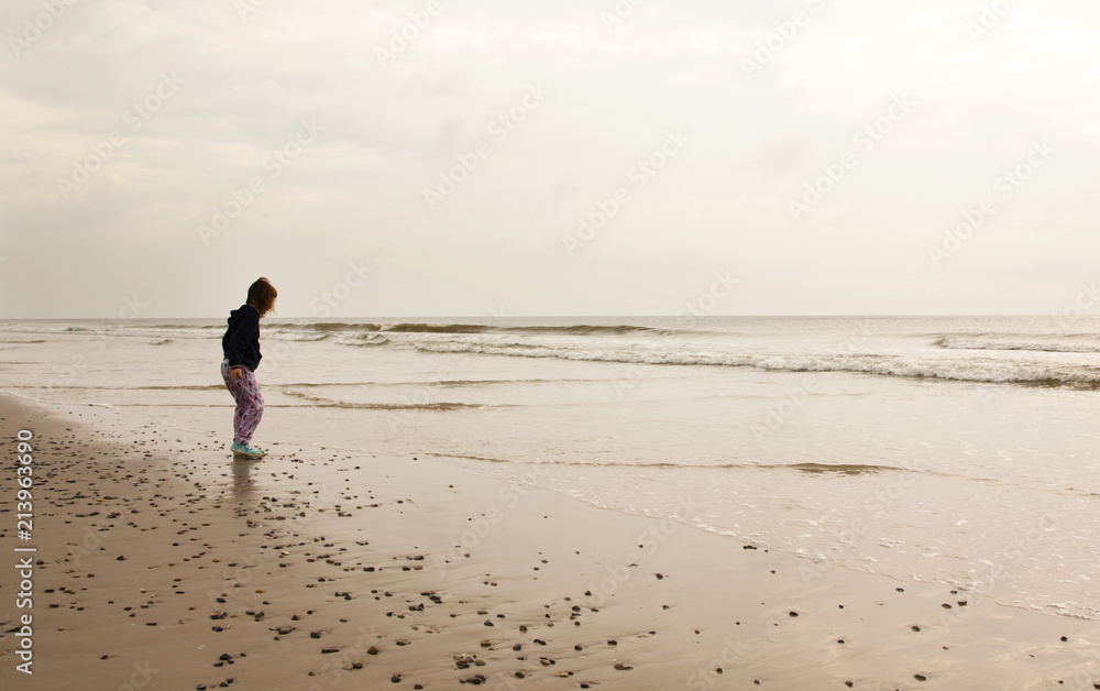 North Sea beach in Denmark at cloudy day. Small girl collecting stones. North Sea beach in Denmark at cloudy day. Small girl collecting stones.