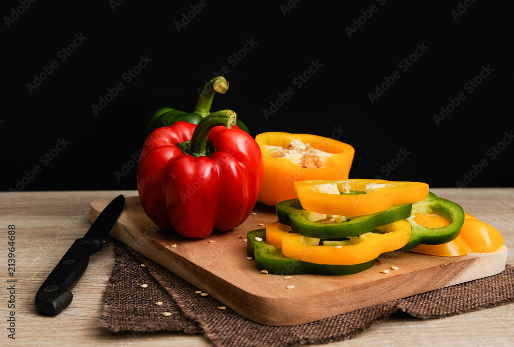 Colourful red,yellow and green peppers are placed on a wooden tray ready for cooking with black background,Bell pepper slice,Selective focus Colourful red,yellow and green peppers are placed on a wooden tray ready for cooking with black background,Bell pepper slice,Selective focus