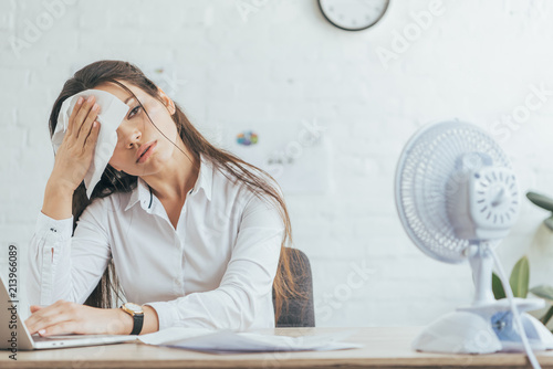 sweaty businesswoman working in office with electric fan