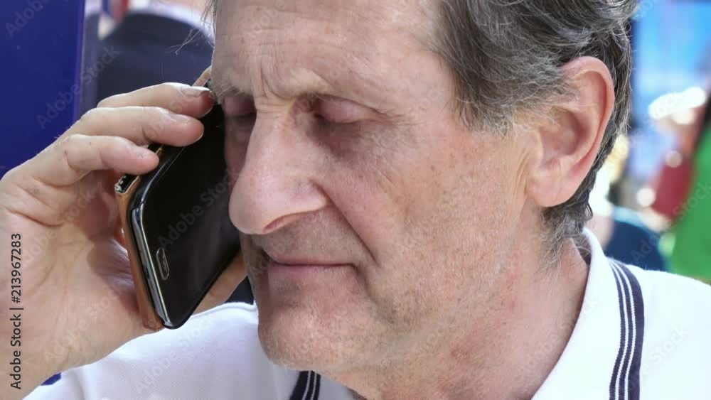 Serious old man in the street talking by phone- sunny day Serious old man in the street talking by phone- sunny day