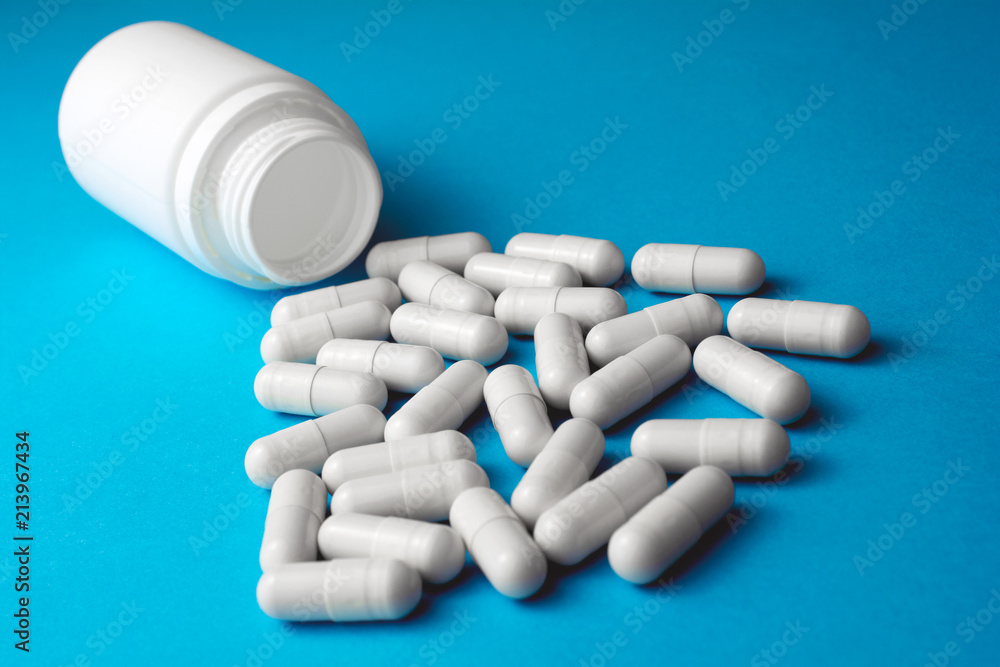 Heap of pills or tablets capsule plastic drugs bottle blue background. Pharmaceutical medicament antibiotic concept.