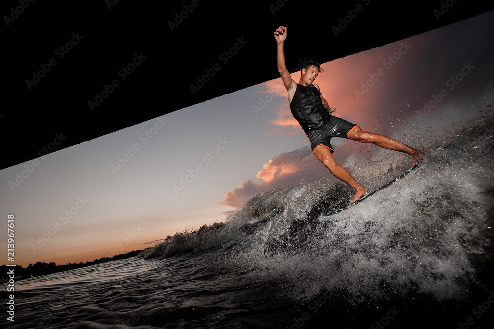 Athletic and young man jumping on wakesurf down the river waves at the sunset Athletic and young man jumping on wakesurf down the river waves at the sunset