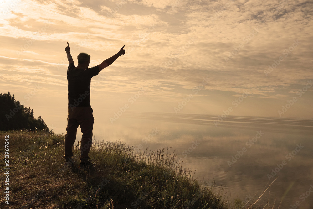 A man stands on top of a mountain and sees the view of nature. The tourist raises his hands and enjoys the fresh air. A man stands on top of a mountain and sees the view of nature. The tourist raises his hands and enjoys the fresh air.