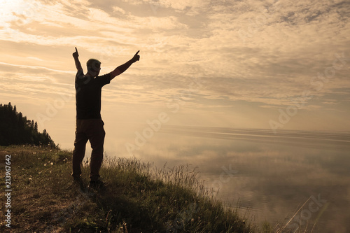 A man stands on top of a mountain and sees the view of nature. The tourist raises his hands and enjoys the fresh air.