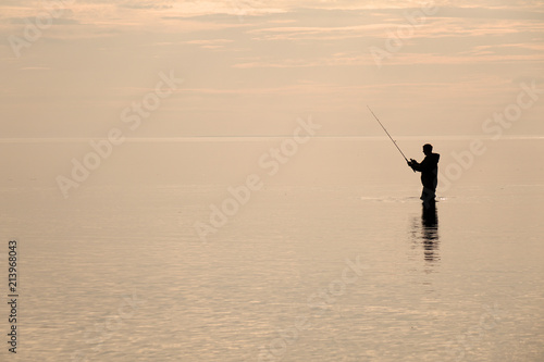 Silhouette of a fisherman at sunset. Fishing on the lake.