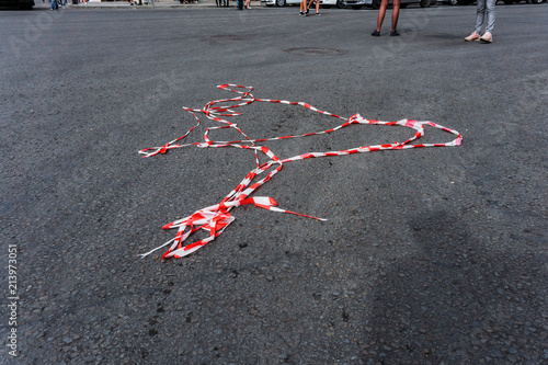 Red white protective tape carried away by the wind is lying under your feet passer-by on the asphalt on the road during a mass holiday