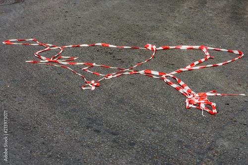 Red white protective tape carried away by the wind is lying under your feet passer-by on the asphalt on the road during a mass holiday