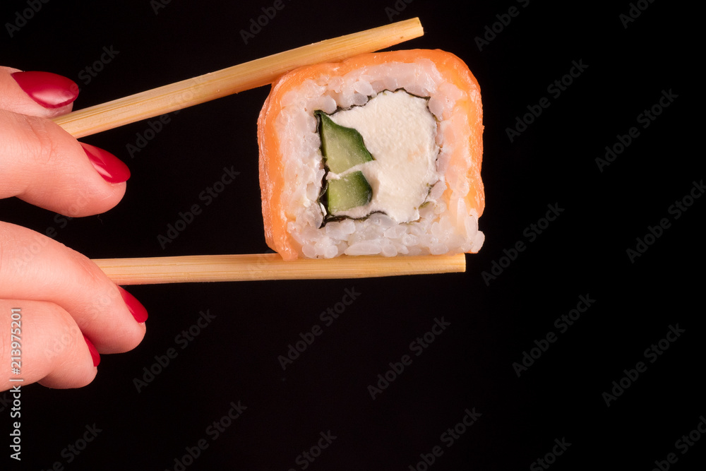 Japanese food. Rolls sticks isolated on a black background. Woman hand with red nail polish holding one sushi roll with cucumber and salmon. Japanese food. Rolls sticks isolated on a black background. Woman hand with red nail polish holding one sushi roll with cucumber and salmon.
