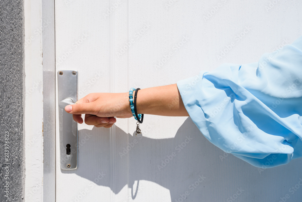 Hand holds doorknob on wooden front door