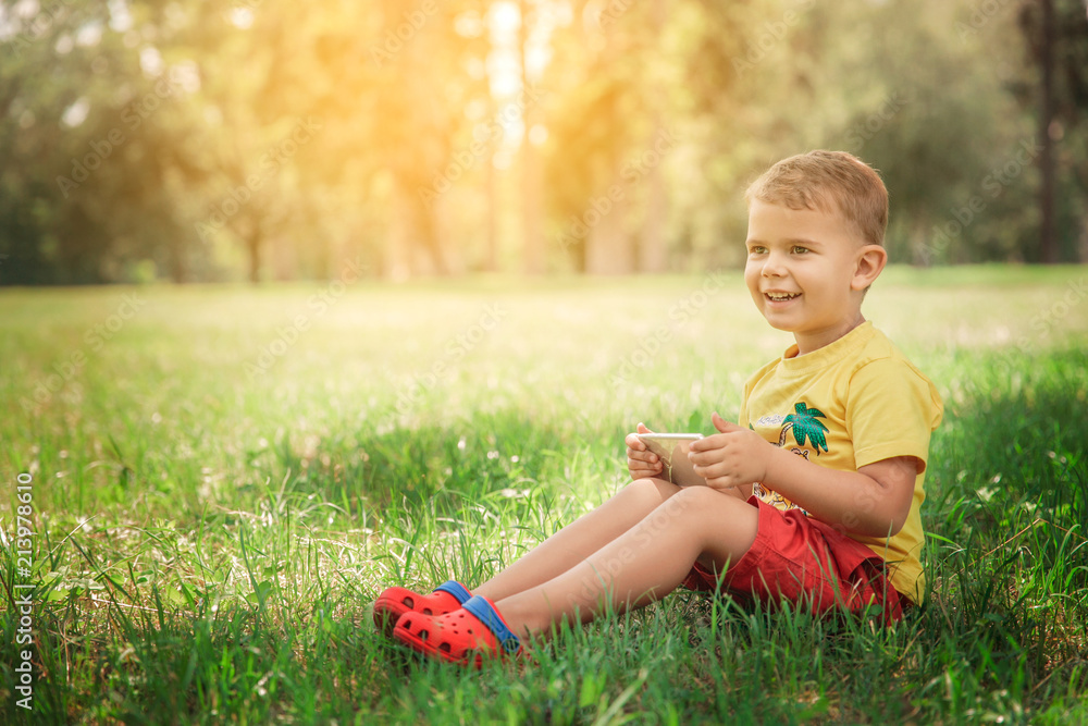 A little boy is sitting with the phone on the grass. A little boy is sitting with the phone on the grass.