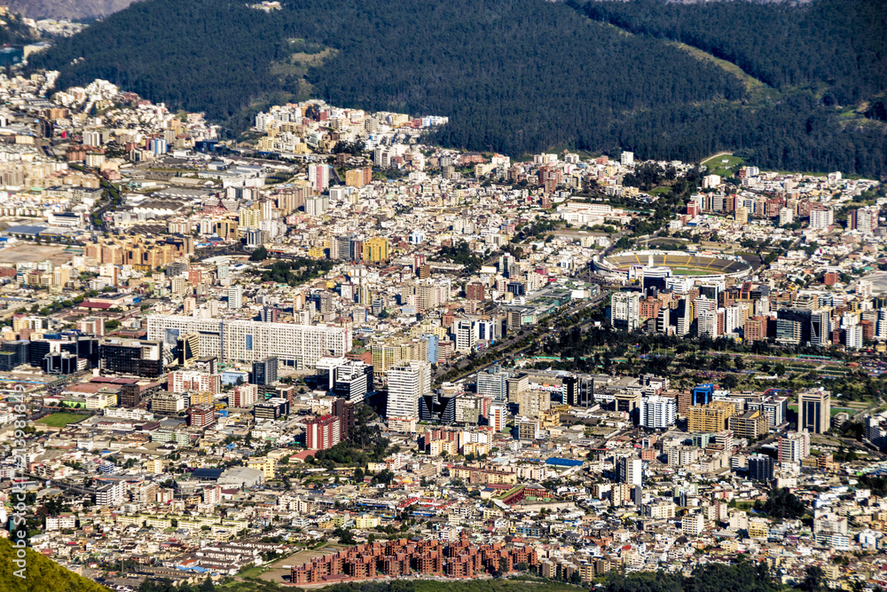 A panoramic view from higher ground of the city of Quito, capital of Ecuador. Buildings, houses and the mountains can be seen in the back. It's a sunny day with blue sky. photo taken from El Panecillo