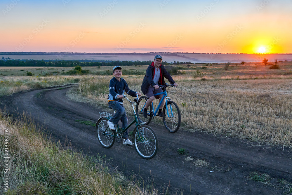Obraz premium father and son ride a bike in the country on the field in the evening