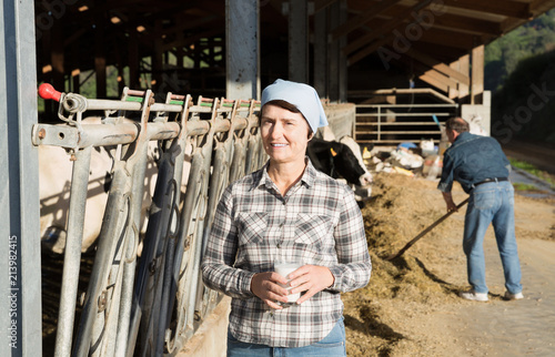 Smiling mature female farmer with cow milk in glass