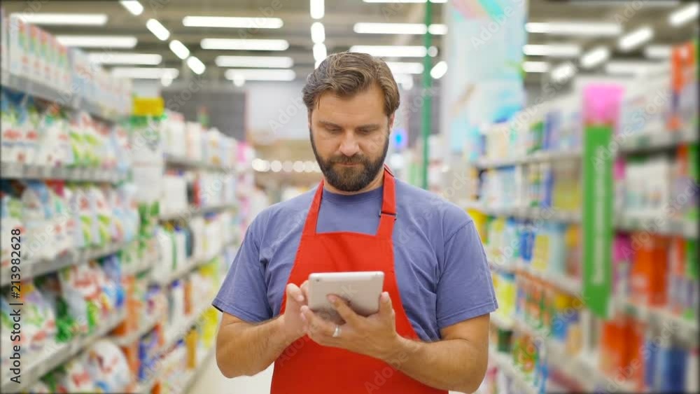 Handsome salesman using digital tablet standing among shelves In supermarket Handsome salesman using digital tablet standing among shelves In supermarket