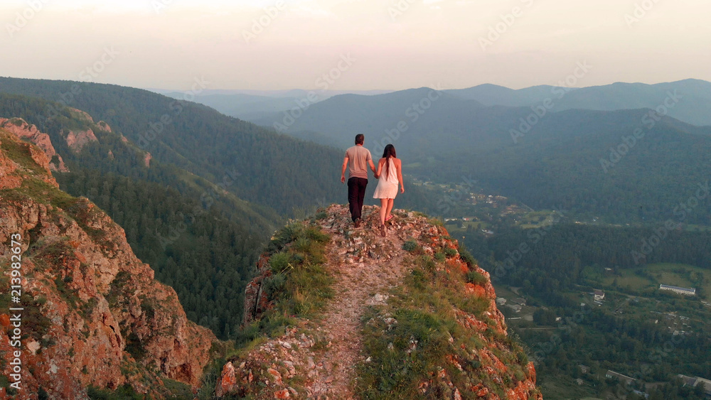 A man and a woman stand on top of the mountain at sunset.