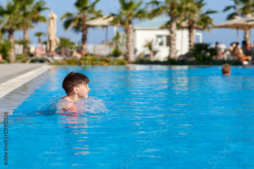 Caucasian boy in floating sleeves swimming in pool at resort.