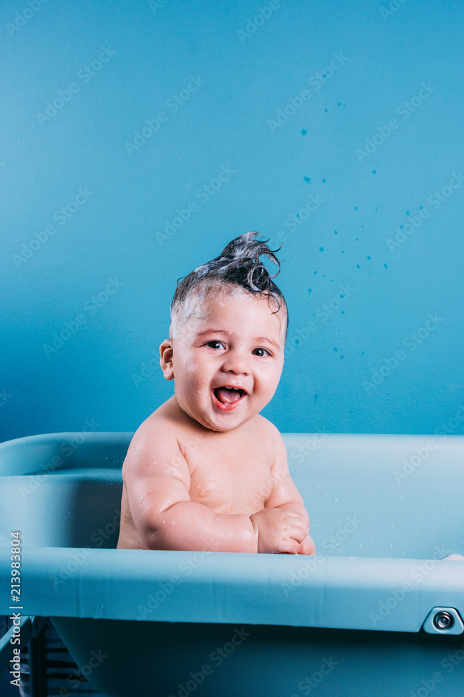 Happy laughing baby taking a bath. Smiling kid in bathroom with blue colorful background. Hygiene and care for young children. Happy laughing baby taking a bath. Smiling kid in bathroom with blue colorful background. Hygiene and care for young children.
