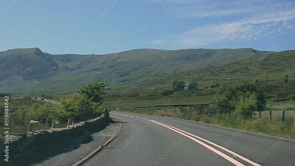 Driving along a mountain road in slow motion surrounded by farmland, mountains and trees Driving along a mountain road in slow motion surrounded by farmland, mountains and trees