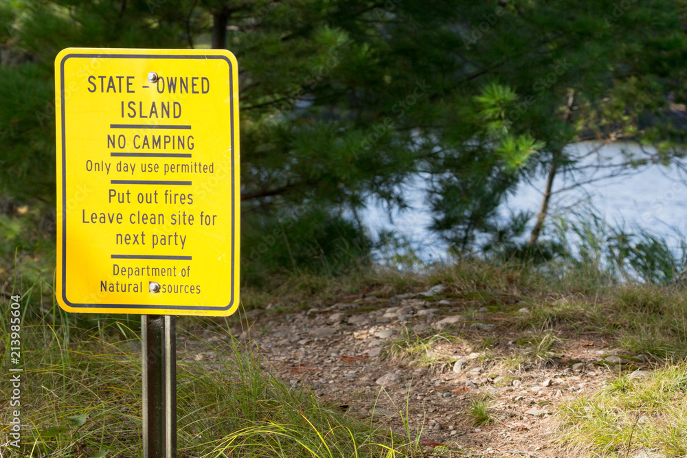 Yellow sign says State-Owned Island, no camping, day use only, put out your fire, and clean up after yourself, from the Department of Natural Resources.