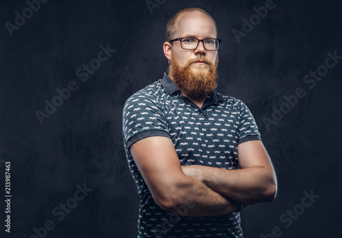 Portrait of a redhead bearded male dressed in a t-shirt posing with crossed arms. Isolated on dark textured background.