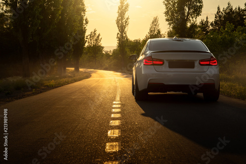 White car is parked on empty countryside asphalt road at sunset © Ivan Kurmyshov