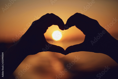 Hands in the shape of heart against the background of the sunset by the sea.