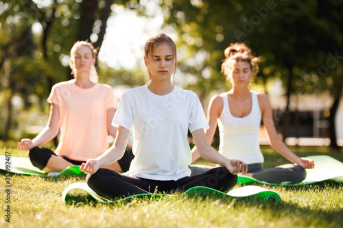 Group of young women practicing yoga, morning meditation in nature at the park