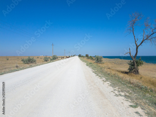 White road along blue sea / White road along coast of blue sea in sunlight on hot summer day