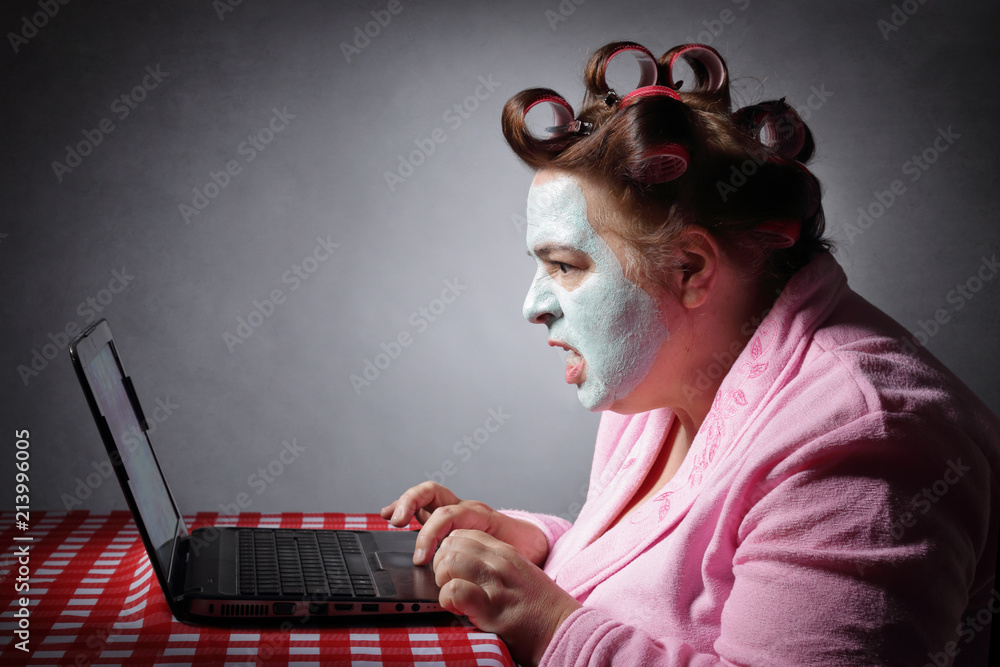femme ronde drôle en peignoir et bigoudis devant son ordinateur portable  Photos | Adobe Stock