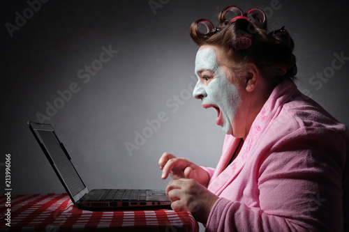 femme ronde drôle en peignoir et bigoudis devant son ordinateur portable