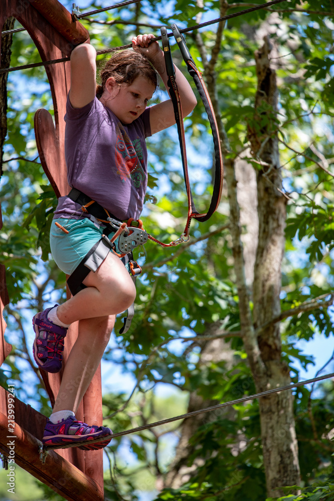 Portrait of a beautiful girl on a rope park among trees. Children summer activities.