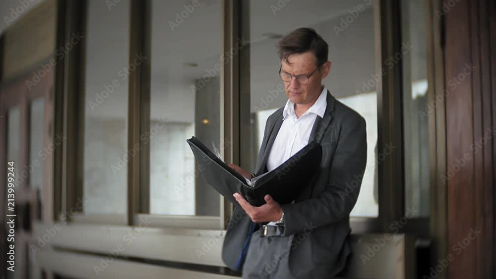 a young, respectable businessman sent to an office building. In his hands he holds a briefcase, looks through documents. a young, respectable businessman sent to an office building. In his hands he holds a briefcase, looks through documents.