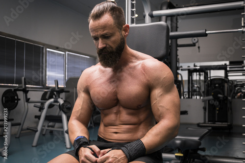 Hombre fuerte con grandes músculos descansando entre serie y serie mientras entrena en el gimnasio.