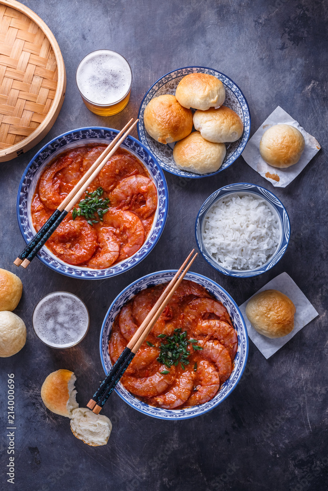 Spicy asian shrimps in tomato sauce with rice, buns and beer, top view