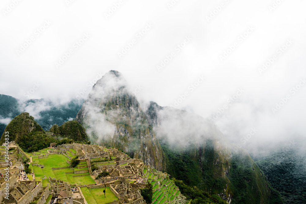 Fototapeta premium Panoramic view of Machu Picchu with Huayna Picchu mountain covered with clouds