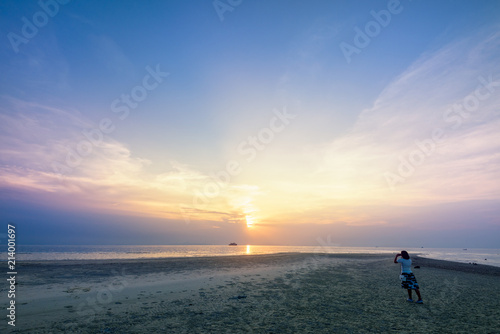 Asian woman tourist taking photo on the beach and beautiful natural landscape of colorful sky and sea during a sunset at Nathon Sunset Viewpoint in Samui island, Surat Thani, Thailand